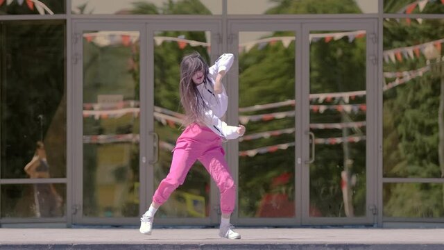 Talented girl performing cool dance in front of the building. Concept of learning hip hop and break dance technique. Youth subculture. Contemporary choreography. Slow motion