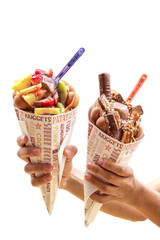Naklejka na ściany i meble Bubble waffles with ice-cream, fruits, chocolate held in hands on a white background
