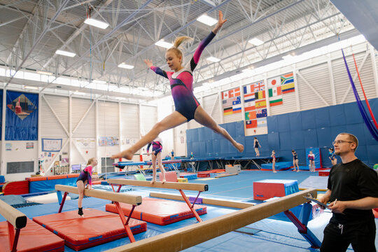 Girl leaping on balance beam in gym