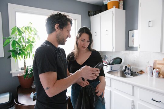 Man And Woman Looking At Phone In Kitchen