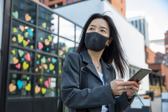 Businesswoman in face mask with smart phone waiting for ride share