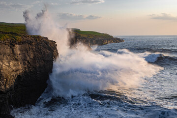 Big waves crashing against the cliffs at sunset