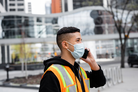 Male construction worker in face mask talking on smart phone in city