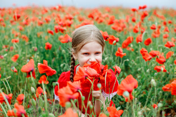 a girl of European appearance with two pitails in a red dress stands in a beautiful poppy field against 