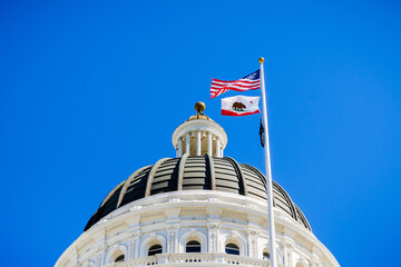 The US and the California state flag waving in the wind in front of the dome of the California State Capitol, Sacramento, California