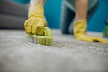 Close up of housewife in yellow rubber gloves cleaning carpet from spots with brush. Concept of...