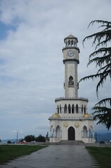 Obraz premium White tower with clocks, columns and domes, paved walkway, tree branch against a cloudy sky 