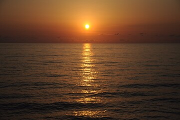 Obraz premium Sunset sun on an almost clear sky with milky clouds and a golden path on the surface of a calm sea