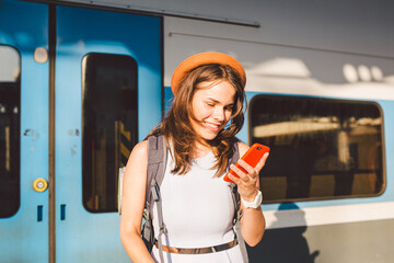 Smiling woman using smart phone on station. Young woman holding smartphone and standing at train...