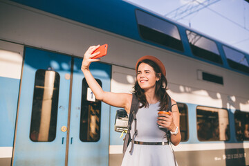 Theme travel, travel by rail. Beautiful caucasian woman in dress and backpack uses phone near...