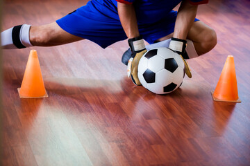 Ball in hands of futsal goalkeeper on wooden futsal floor. Indoor soccer sports hall. Asian futsal player, Sports background. Youth futsal league. Indoor football players.