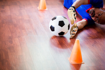 Ball in hands of futsal goalkeeper on wooden futsal floor. Indoor soccer sports hall. Asian futsal player, Sports background. Youth futsal league. Indoor football players.