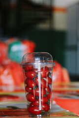 Plastic cup with cherry tomatoes against the background of bazaar.