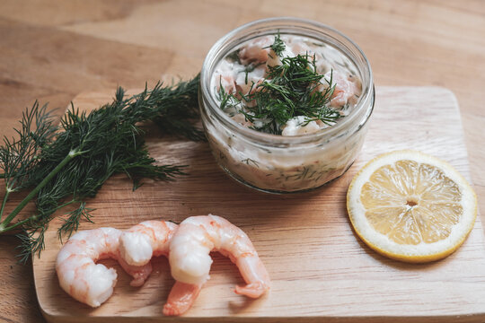 Scandinavian Food - Wooden chopping board with fresh shrimps, dill, slice of lemon and glass jar of traditional Skagen "r&ouml;ra" dip made of mayonnaise, shrimp, and dill. Vintage filter, sepia tones