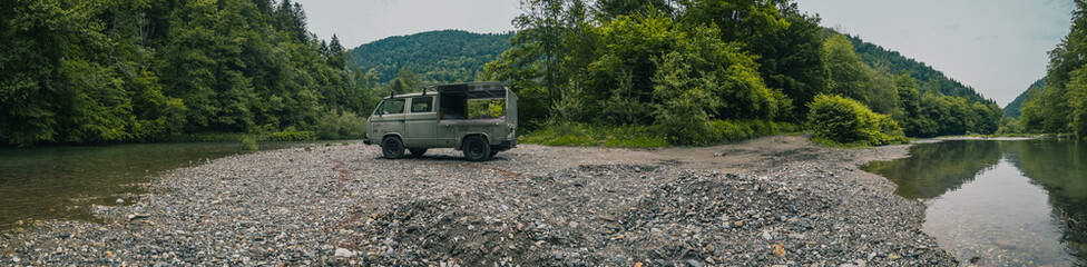 Old vintage custom offroad campervan is parked in the morning hours on the shores of a lazy river...