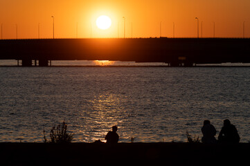 Fototapeta premium Silhouettes of people enjoying seascapes on the shore during sunset.