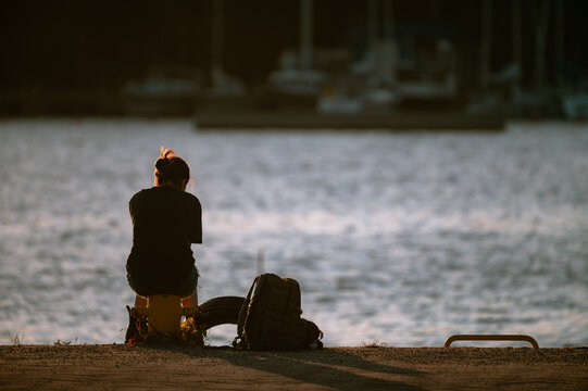 Alone female sitting on a bollard at the shore looking at the sunset.