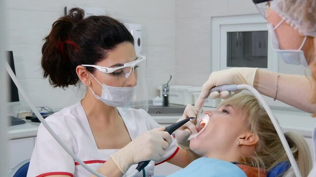 Professional stomatologist and dental assistant working with patient. Air flow method of cleaning teeth with sandblasting machine. Wahing mouth with irrigator