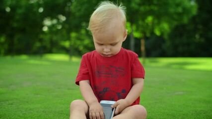 Toddler sitting in green meadow with phone. Cute child holding cellphone