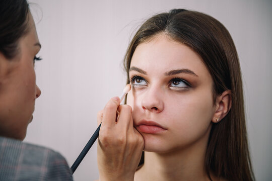 Visagiste doing make-up for beautiful teenage girl, using eyeliner or bright concealer under eyes. Make up, cosmetics, beauty standards, skin care concept. Close up shot.