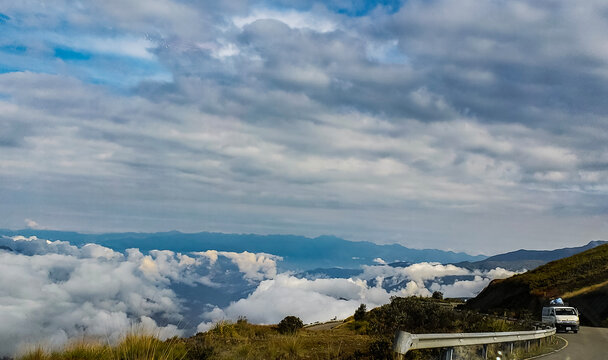 White car on a road with fonfo mountains and cloudy sky.