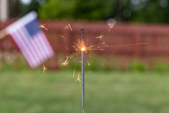 Closeup of burning sparkler and American flag in backyard. Concept of fireworks safety, Independence Day and Fourth of July celebration