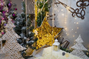 Wooden star with golden sequins, unfocused white lanterns and candle standing on shiny sparkling fabric. Fir branches, festive Christmas and New Year decorations. Winter magic and holidays.