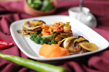 Fried chicken with vegetables. Pepper, broccoli, eggplant, paprika and potatoes. A dish on a red background.