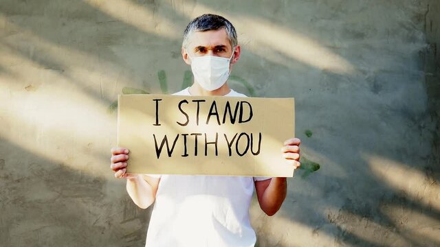 Gray-haired man in a mask with a cardboard poster in his hands with the inscription - I STAND WITH YOU. One protest