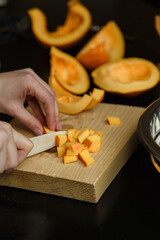 Woman chopping pumpkin on kitchen board, only hands visible. Autumn seasonal vegetables cooking. Healthy eating habits, organic vegetarian food concept.