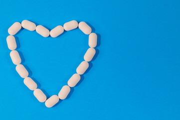 
white long pills laid out in the shape of a heart on a blue background and with place for text on the right, close-up top view.