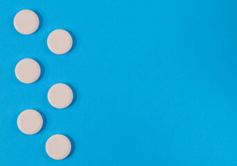 six round, large white pills on the left on a blue paper background and with place for text on the right, close-up top view.