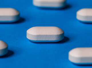 one white and long pill close-up in the middle and five tablets at the edges on a blue background, side view.