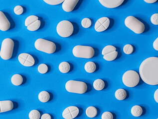 many different pills  scattered on a blue paper background, close-up top view.