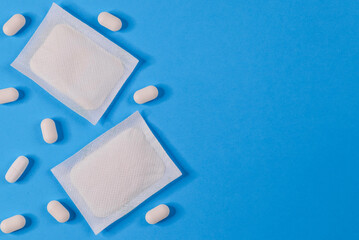 
Two medical adhesive plasters and pills around them lie on the left and with room for text on the right, close-up top view.