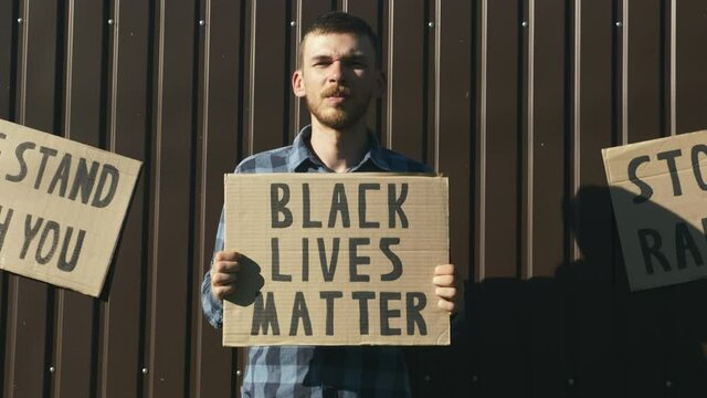 Portrait of young caucasian man holding sign "Black lives matter" in hands. Rally against police brutality. Stop racism. Poster "Black lives matter" in hands of man. Peaceful anti-black racism protest