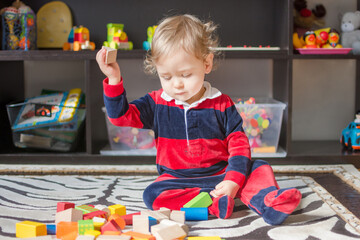 Cute little baby boy having fun at home playing with colorful wooden blocks, on the floor.