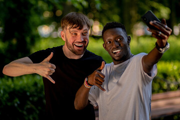 A black man and a white man take selfies on their smartphones and make faces . Interracial...