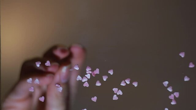 Woman hands throwing pink heart shaped glitter confetti on flat transparent surface. Concept. Bottom view of female hand putting tiny hearts on glass table.