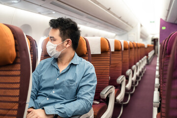Asian traveler business man sitting on seat wearing mask on airplane.