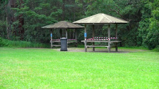 A picknic area on a clearing of a forest with wooden tables and a shed closed due to covid-19 restrictions. Warning tabels block the entrance.
