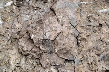 cracked stone wall covered with brown clay and sand