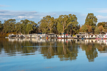 Fototapeta na wymiar The reflection of house boats and tree on a calm river murray located in the river land at Berri South Australia on 20th June 2020
