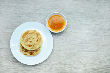 View from above of Roti Canai in a plate and dhal sauce on wooden table 