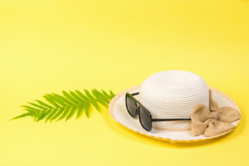 A hat with a bow and sunglasses and a palm leaf on a yellow background.