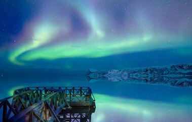 Old wooden pier in the lake on the background Northern lights (Aurora borealis) in the sky over Tromso, Norway