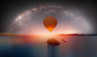 The milky way galaxy over the sea and  silhouette of rock in the night sky - Hot air balloon flying over night sea