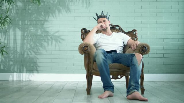 barefoot man in a t-shirt and jeans in a leather crown sits in an armchair