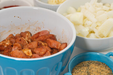 Marinated raw pork meat in a bowl, and some vegetables on a kitchen table, close up on white background