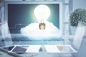 Computer on desktop in office with bulb icon hologram. Double exposure. Concept of idea.